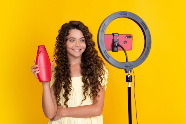 Adolescent enregistrant une vidéo multimédia en ligne en tenant un après-shampooing ou une bouteille de shampoing