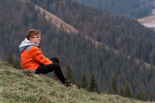 Un adolescent est assis sur une colline et regarde au loin pense à quelque chose Week-end Voyager avec des enfants