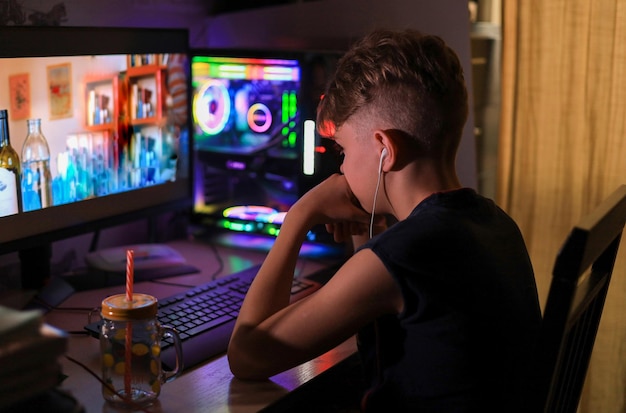Un adolescent est assis avec des écouteurs devant un écran d'ordinateur et regarde une vidéo dans l'obscurité