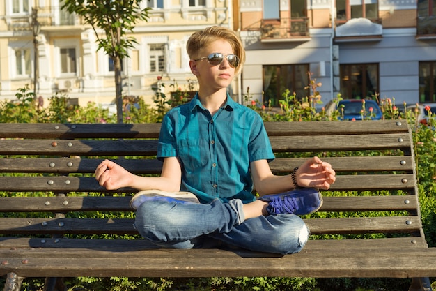 Adolescent est assis en posture de lotus sur un banc dans le parc de la ville. Détendez-vous, reposez-vous, méditez.