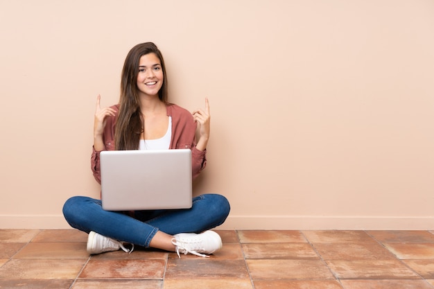 Adolescent étudiant fille assise sur le sol avec un ordinateur portable pointant vers le haut une bonne idée