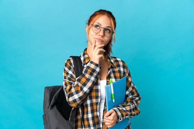 Adolescent étudiant fille russe isolée sur mur bleu ayant des doutes tout en levant les yeux