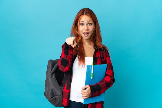 Photo adolescent étudiant fille russe isolée sur mur bleu surpris et pointant vers l'avant