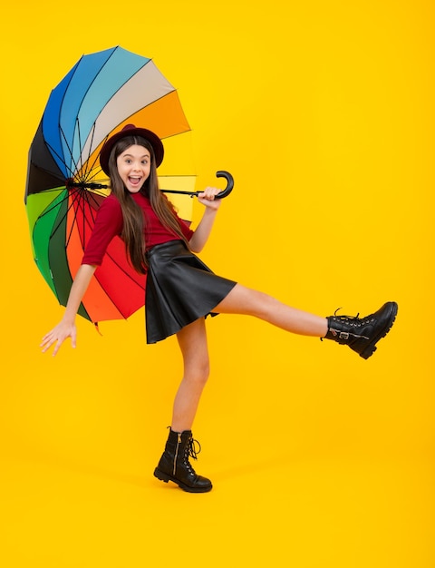 Adolescent excité étonné émotions ravies Mode automne enfants météo Enfant adolescent fille avec parapluie en jupe bottes et chapeau isolé sur fond jaune Automne vêtements à la mode saison d'automne