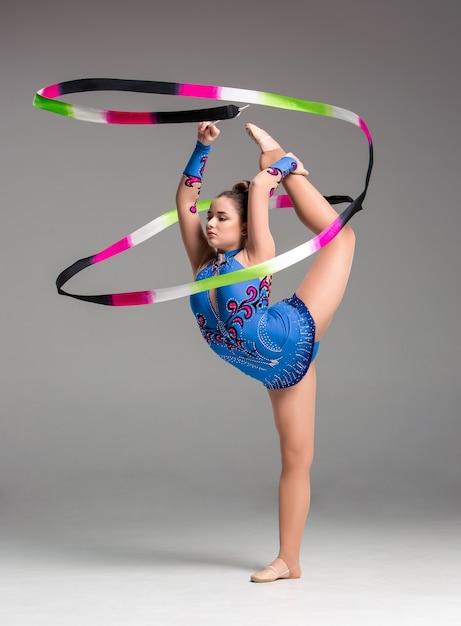 Adolescent faisant la danse de gymnastique avec le ruban coloré sur un fond gris