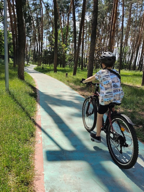Un adolescent fait du vélo dans le parc sur un chemin sinueux en perspective Vue arrière