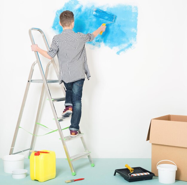 Un adolescent fait des réparations à la maison Peinture de couleur bleue mur avec rouleau à la main Enfant sur échelle Mur pour l'espace de copie de texte