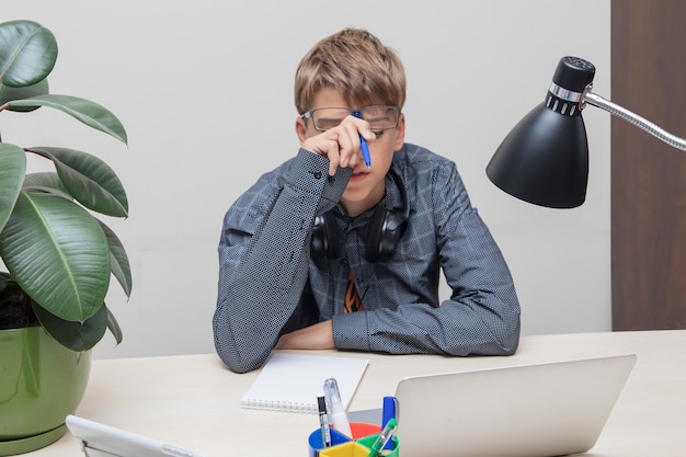 Adolescent fatigué avec des lunettes et des écouteurs avec un stylo à la main