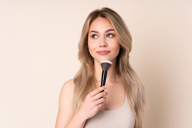 Adolescent femme blonde avec pinceau de maquillage sur mur isolé