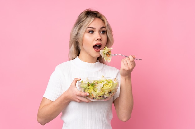 Adolescent femme blonde tenant une salade sur mur rose