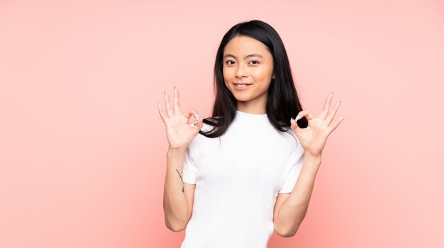 Adolescent femme chinoise isolée sur mur rose montrant signe ok avec deux mains