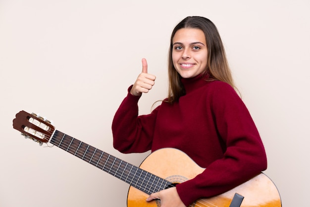 Adolescent femme avec guitare sur mur isolé avec les pouces vers le haut parce que quelque chose de bien s'est produit