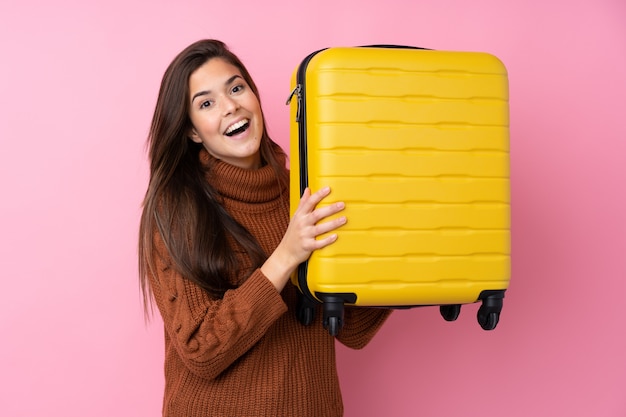 Adolescent femme sur mur rose isolé en vacances avec valise de voyage et surpris