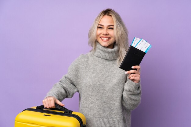 Adolescent femme sur mur violet isolé en vacances avec valise et passeport