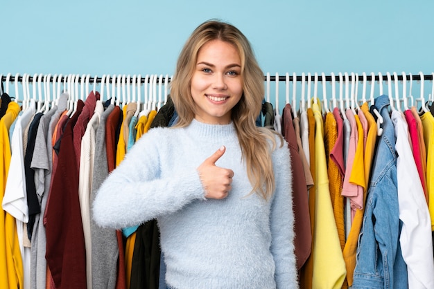 Adolescent femme russe acheter des vêtements isolés sur le mur bleu donnant un coup de pouce geste