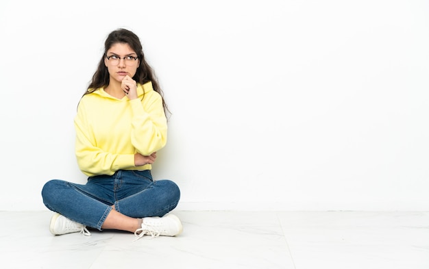 Adolescent femme russe assise sur le sol ayant des doutes et de la pensée
