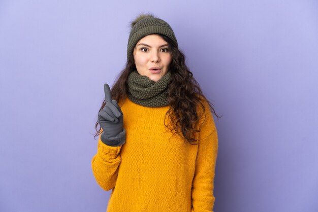 Adolescent femme russe avec chapeau d'hiver isolé sur mur violet dans l'intention de réaliser la solution tout en soulevant un doigt