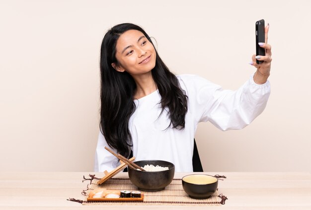 Adolescent fille asiatique manger de la nourriture asiatique sur un mur beige faisant un selfie