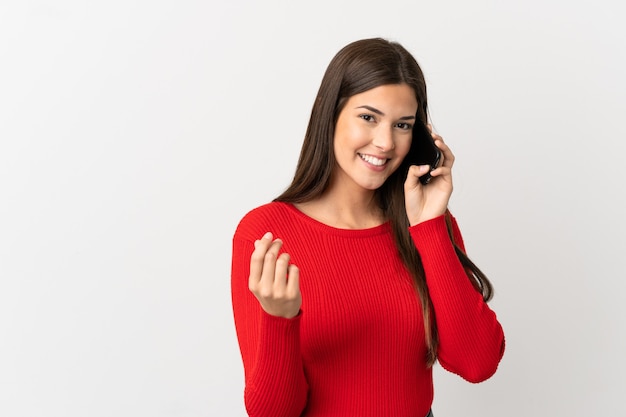 Adolescent fille brésilienne à l'aide de téléphone mobile sur fond blanc isolé faisant le geste de l'argent