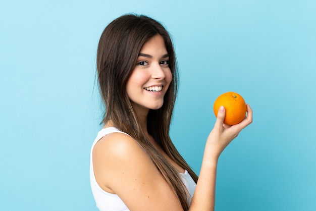 Adolescent fille brésilienne sur fond bleu isolé tenant une orange