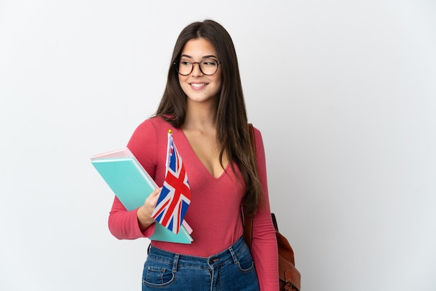 Adolescent fille brésilienne tenant un drapeau du Royaume-Uni isolé sur fond blanc à la recherche sur le côté et souriant