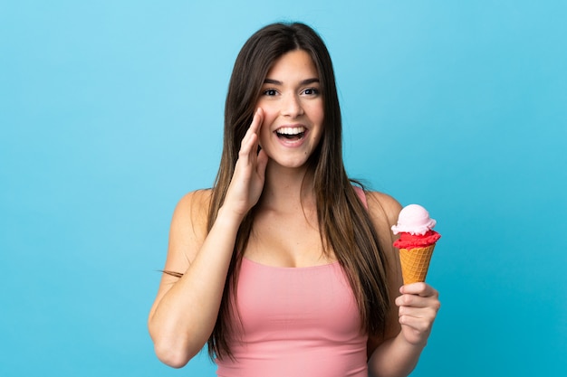 Adolescent fille brésilienne tenant une glace au cornet sur fond bleu isolé criant avec la bouche grande ouverte