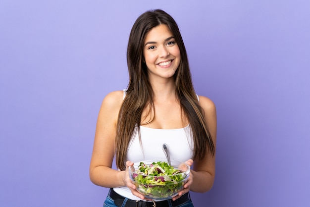 Adolescent fille brésilienne tenant une salade sur un mur violet isolé