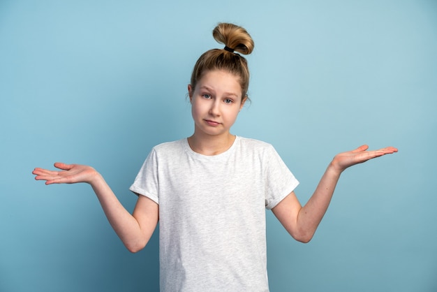 Adolescent fille confuse à bras ouverts sur un mur bleu