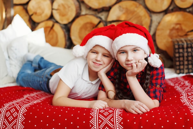 Adolescent fille et garçon dans un chapeau de Noël rouge parlant, allongé sur le lit dans un intérieur festif
