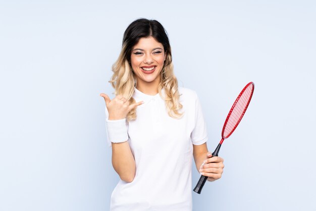 Adolescent fille jouant au badminton sur mur bleu faisant geste de téléphone