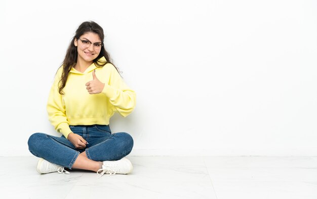 Adolescent fille russe assise sur le sol en donnant un geste de pouce en l'air