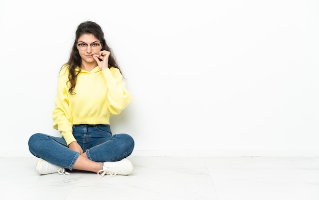 Adolescent fille russe assise sur le sol montrant un signe de geste de silence