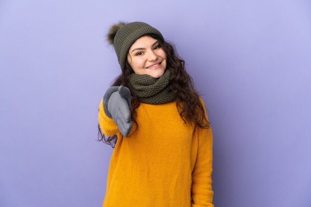 Adolescent fille russe avec chapeau d'hiver isolé sur fond violet se serrant la main pour conclure une bonne affaire