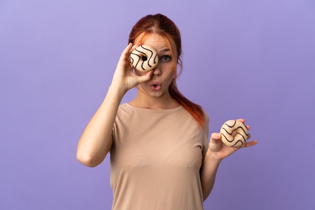 Adolescent fille russe isolé sur fond violet tenant un beignet dans un oeil