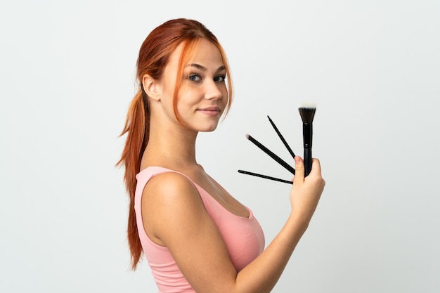 Adolescent fille russe isolée sur un mur blanc tenant un pinceau de maquillage