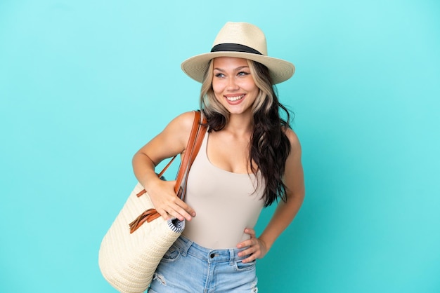 Adolescent fille russe avec pamel et sac de plage isolé sur fond bleu posant avec les bras à la hanche et souriant