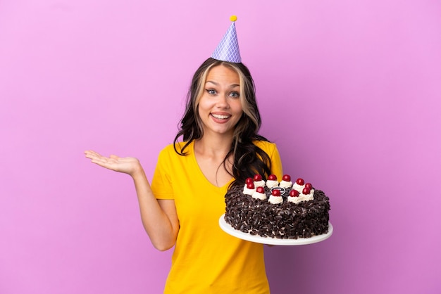 Adolescent fille russe tenant un gâteau d'anniversaire isolé sur fond violet avec une expression faciale choquée