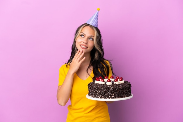 Adolescent fille russe tenant un gâteau d'anniversaire isolé sur fond violet en levant tout en souriant
