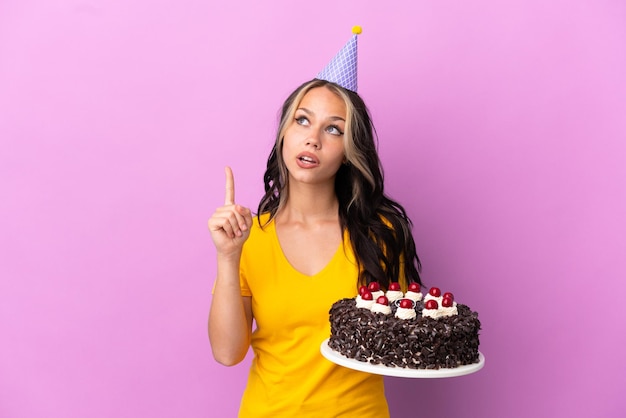 Adolescent fille russe tenant un gâteau d'anniversaire isolé sur fond violet pensant une idée pointant le doigt vers le haut