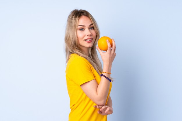 Adolescent fille russe tenant une orange isolé sur fond bleu