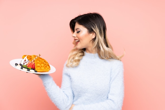 Adolescent fille tenant des gaufres sur mur rose avec une expression heureuse