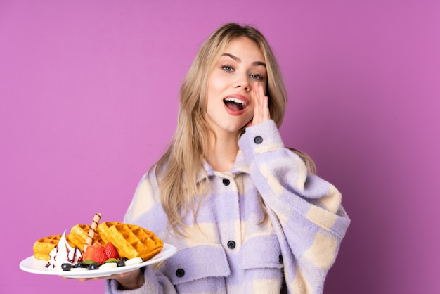 Adolescent fille tenant des gaufres sur un mur violet criant avec la bouche grande ouverte