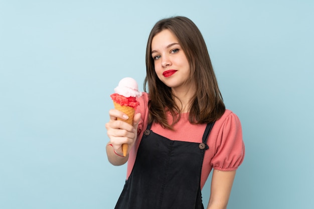 Adolescent fille tenant une glace au cornet isolé sur mur bleu avec une expression heureuse