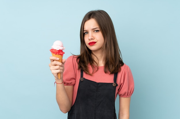 Adolescent fille tenant une glace au cornet isolé sur mur bleu avec une expression triste