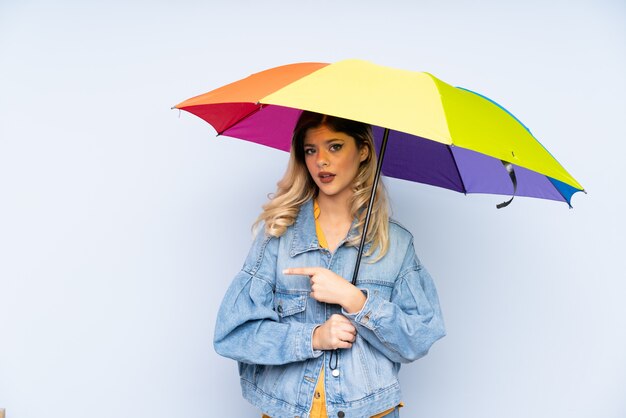 Adolescent fille tenant un parapluie sur le mur bleu et en le pointant