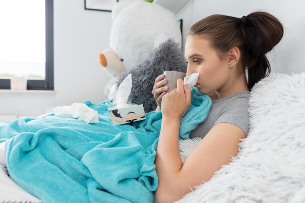 Un adolescent froid déchire son nez dans un mouchoir tout le temps sous une couette chaude