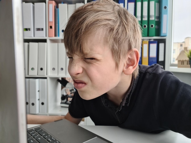 Adolescent garçon louche à l'aide d'un ordinateur portable avec une mauvaise vue assis et regarde l'ordinateur