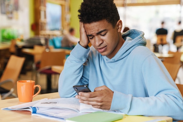 Adolescent garçon sérieux étudiant assis au hub à l'intérieur, à l'aide d'un téléphone portable