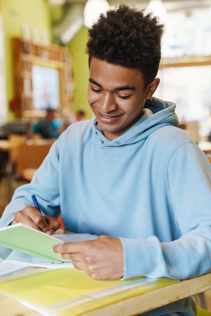 Adolescent garçon souriant étudiant assis au hub à l'intérieur