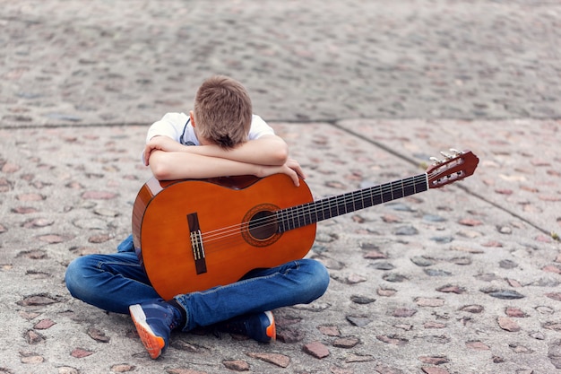 Adolescent avec guitare acoustique et casque assis dans le parc.